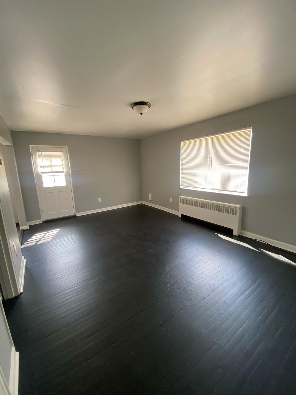 A room with a wooden floor and a window with blinds.