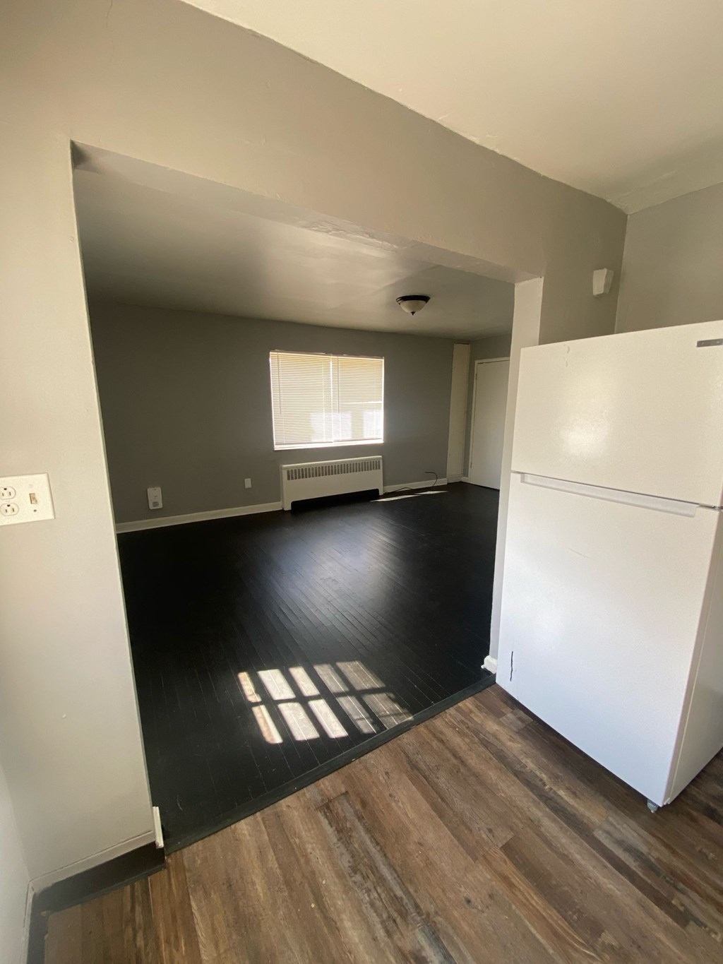 A white refrigerator is in a kitchen with wood flooring.
