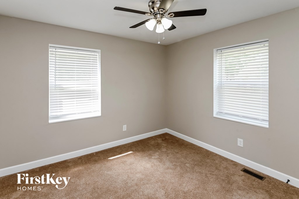 an empty room with a ceiling fan and two windows
