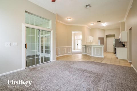 A spacious living room with a grey carpet and a large window.