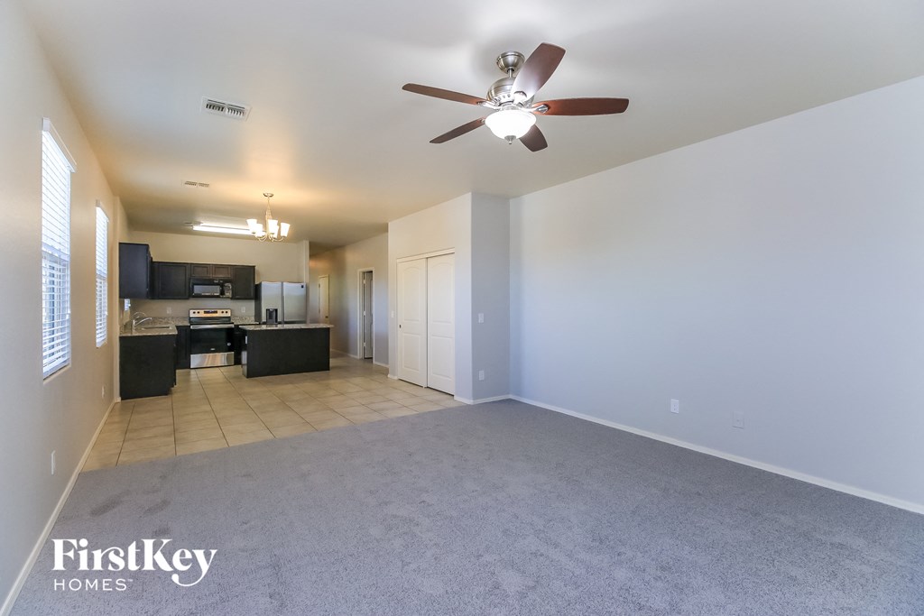A spacious living room with a ceiling fan and a kitchen area in the background.