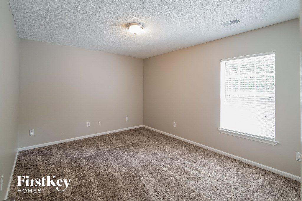 A carpeted room with a window and a FirstKey Homes logo.
