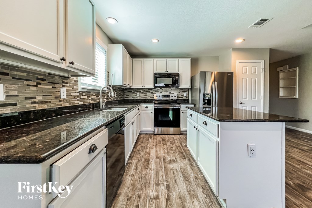 a kitchen with white cabinets and black counter tops and wood floors