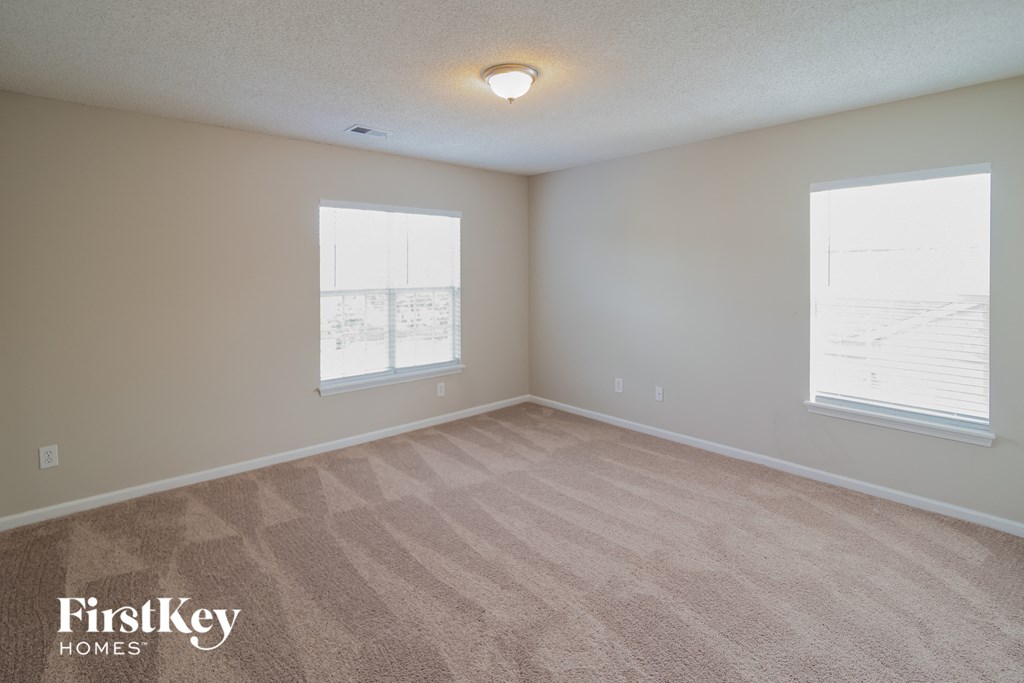 a spacious living room with carpet and two windows