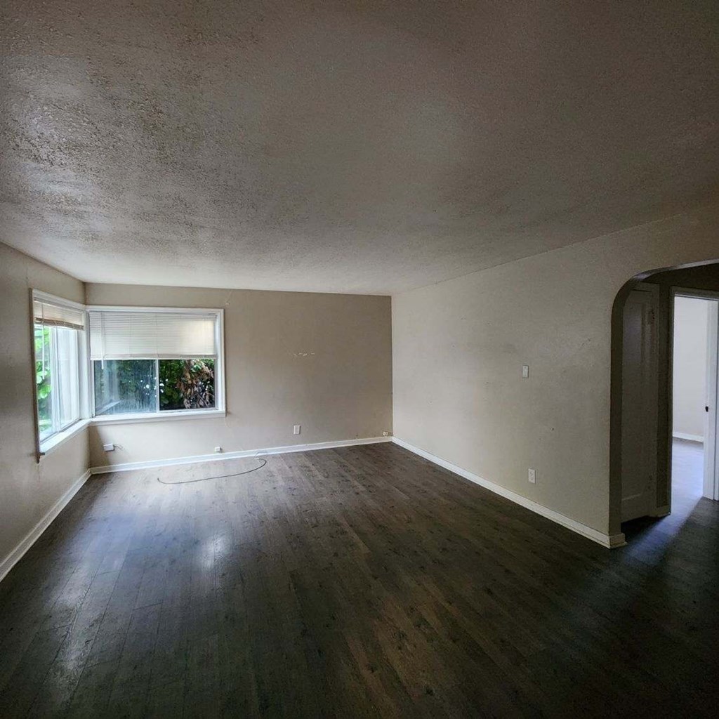 an empty living room with a window and wooden floors