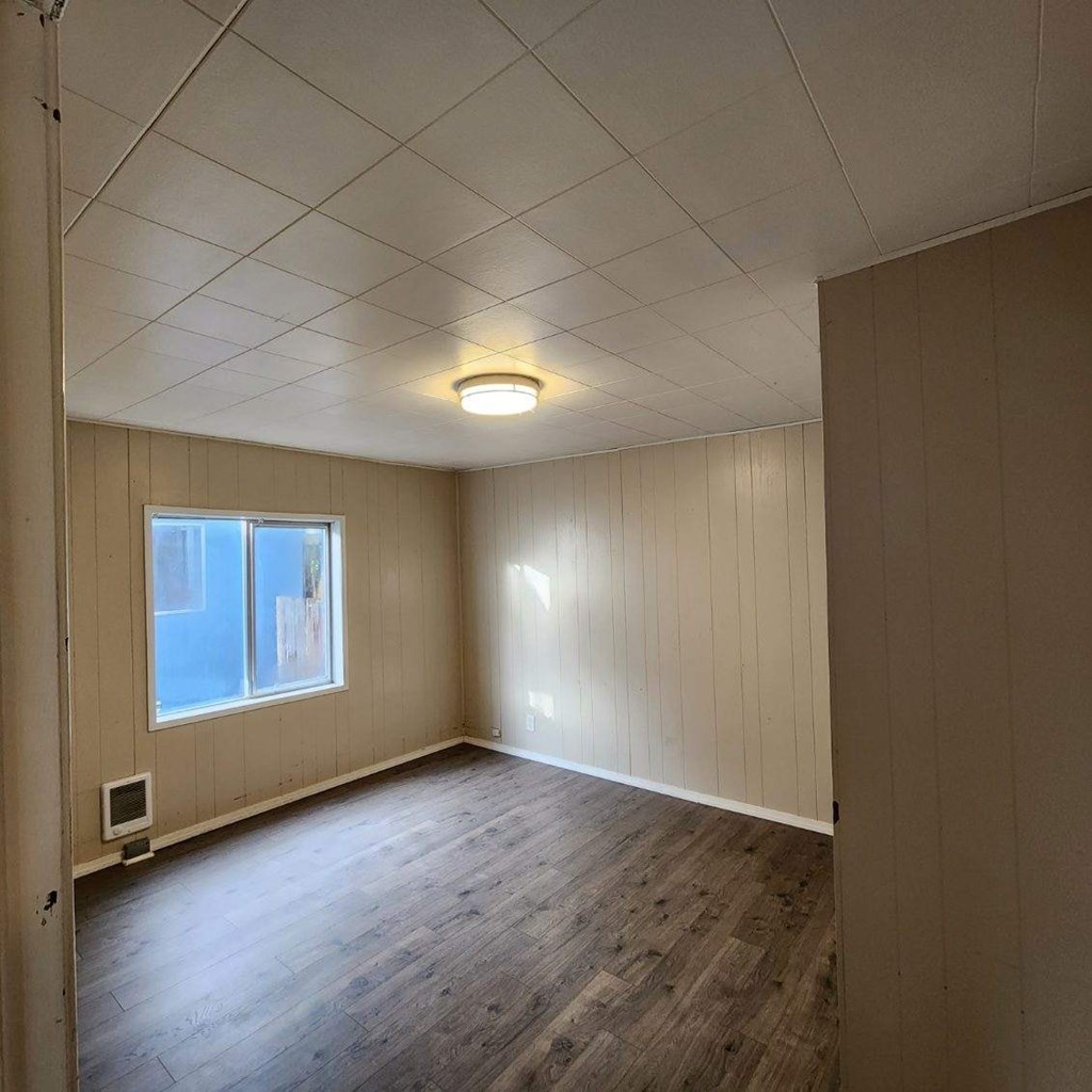 the living room of an empty house with wood floors and a window