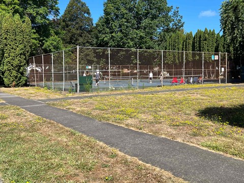 A tennis court surrounded by a fence with people playing tennis.