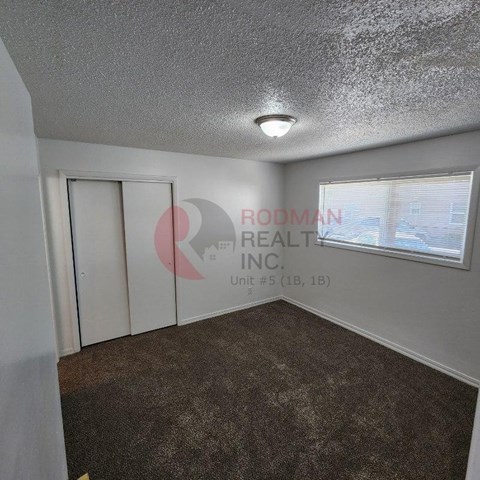 A room with a carpeted floor and a window with blinds.