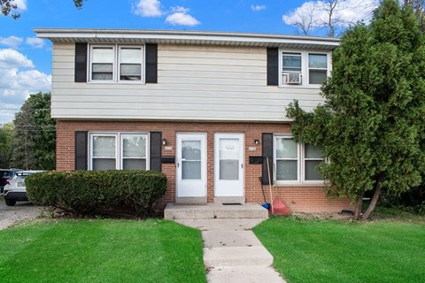 a brick house with two white doors and a lawn