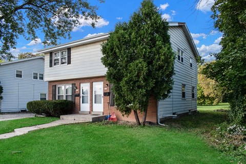 a white and brick house with a tree in the yard