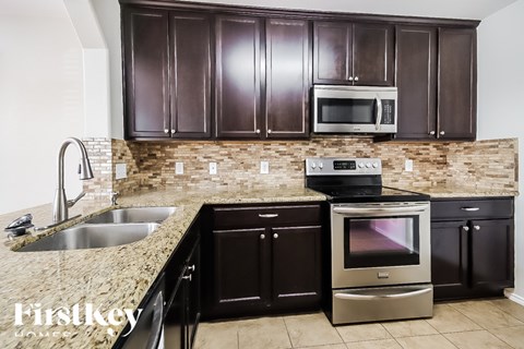 A kitchen with brown cabinets and a stone backsplash.