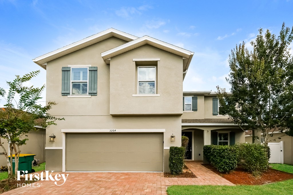 A beige house with a garage door and a brick pathway leading to it.