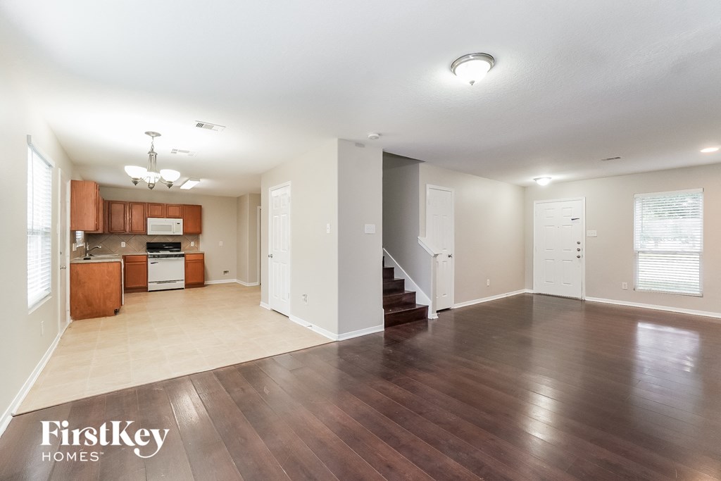 an empty living room with wood flooring and a kitchen