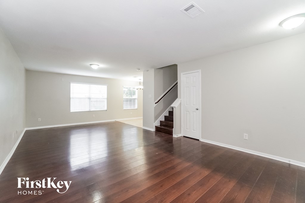 an empty living room with hardwood flooring and a white door to a staircase