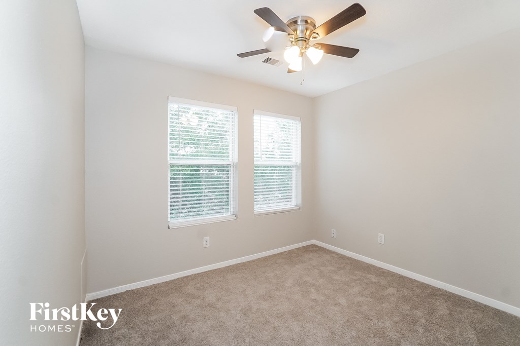 an empty room with a ceiling fan and two windows
