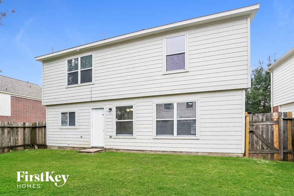 the back of a white house with a yard and a wooden fence