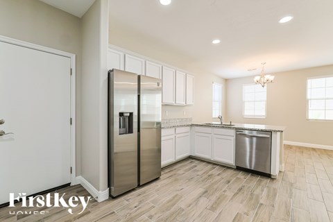 A modern kitchen with a stainless steel refrigerator and wooden flooring.