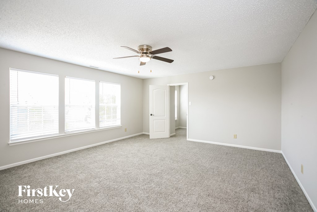 an empty living room with a ceiling fan and three windows
