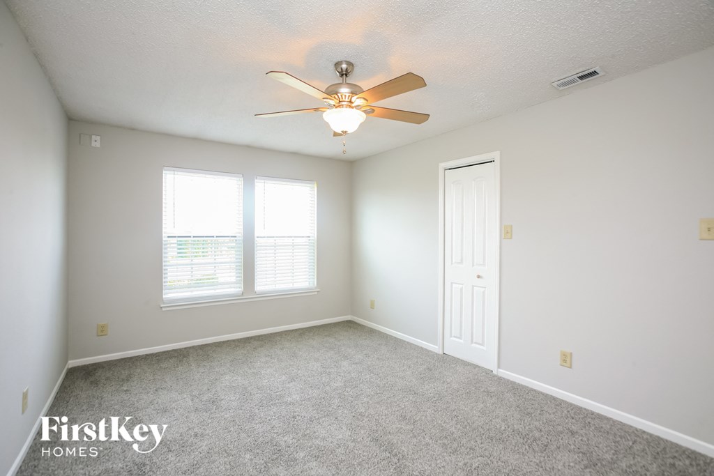 an empty bedroom with a ceiling fan and two windows