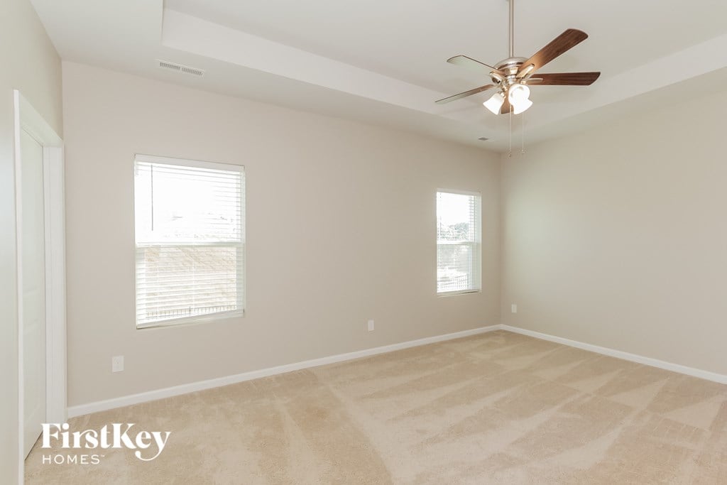an empty living room with a ceiling fan and two windows
