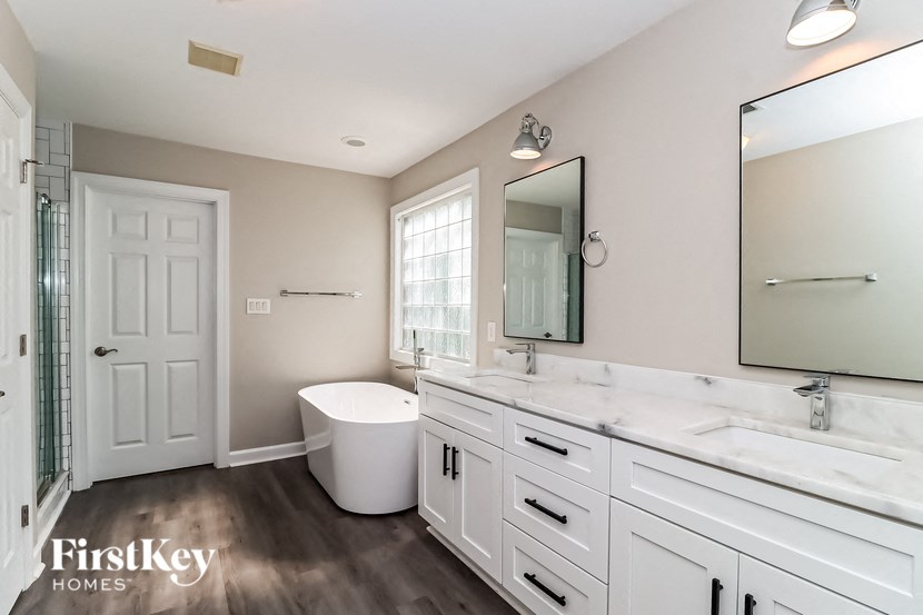a bathroom with white cabinets and a white tub and a sink and a mirror