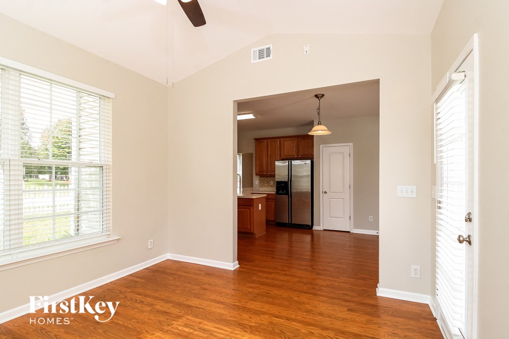 Empty room with wooden floors and a kitchen in the background.