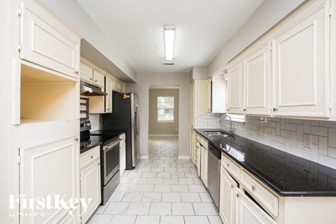 A kitchen with white cabinets and black countertops.