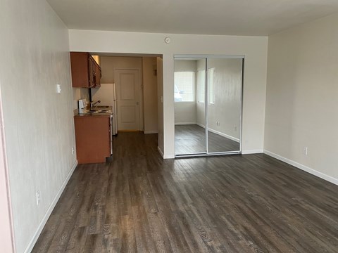 A room with wooden flooring and a kitchenette in the corner.