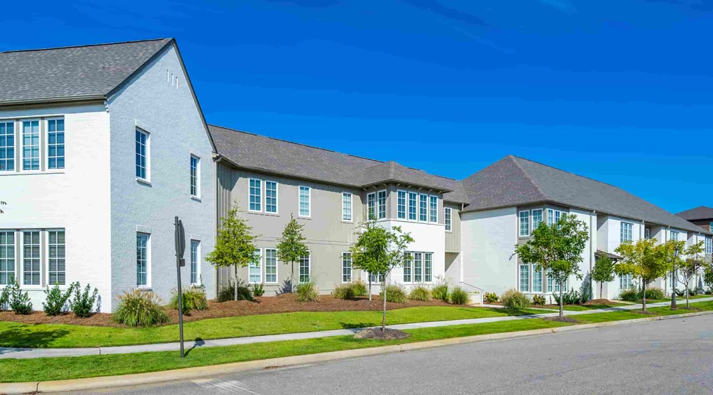 A row of houses with white exteriors and green trees in front.