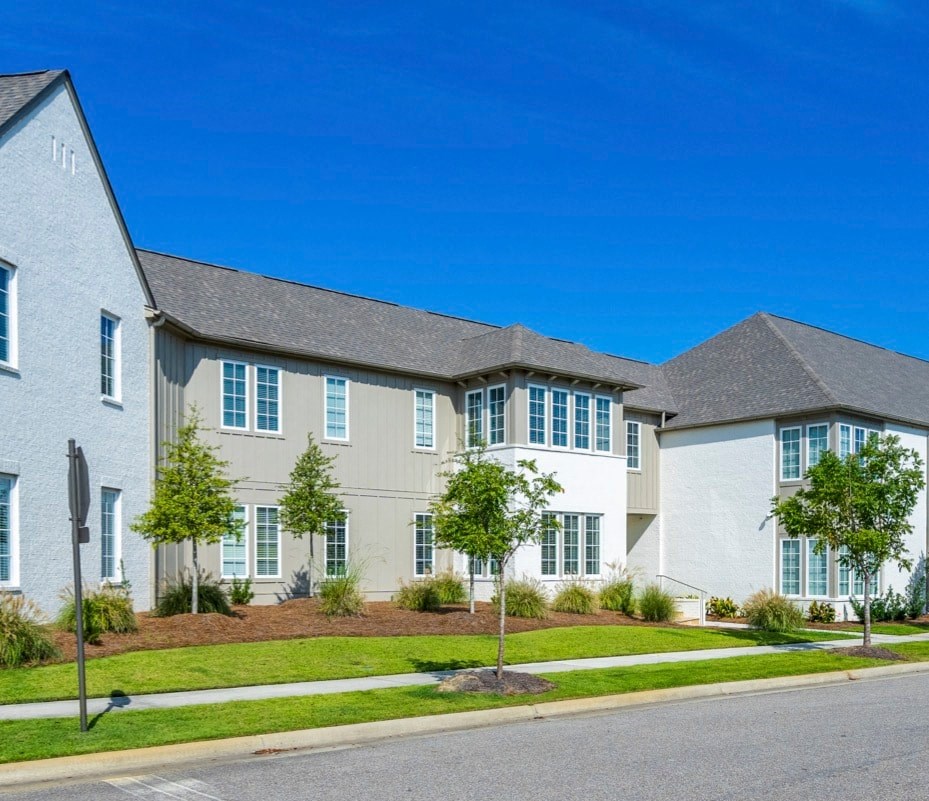 A row of houses with green trees in front.
