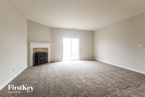 A spacious empty room with a fireplace and a carpeted floor.