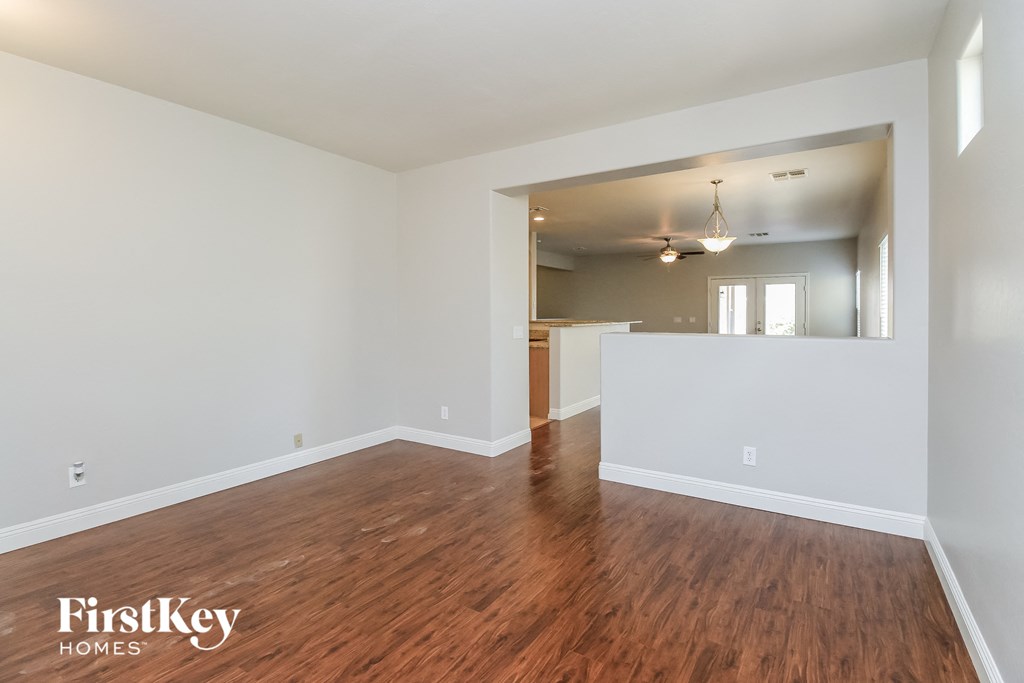 A room with wooden floors and white walls, with a ceiling fan and a door leading to another room.