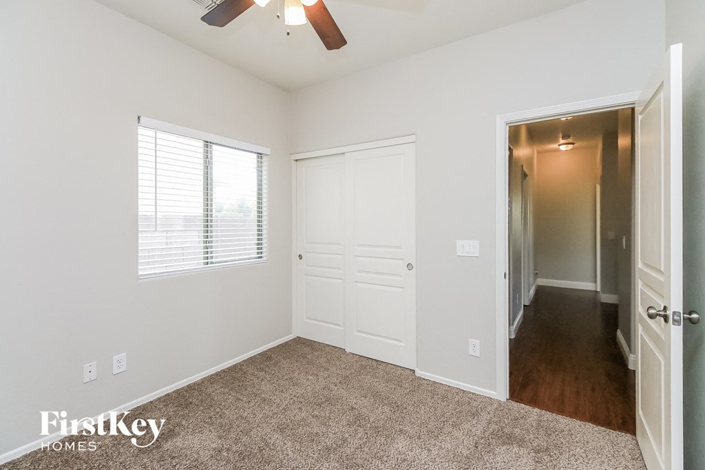 A room with a carpeted floor, a ceiling fan, and a door leading to another room.