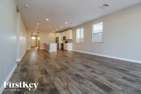 A spacious room with wooden flooring and a kitchen area in the background.