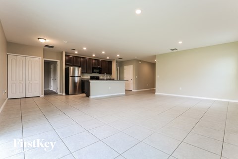 an empty living room with a kitchen with a refrigerator and a sink