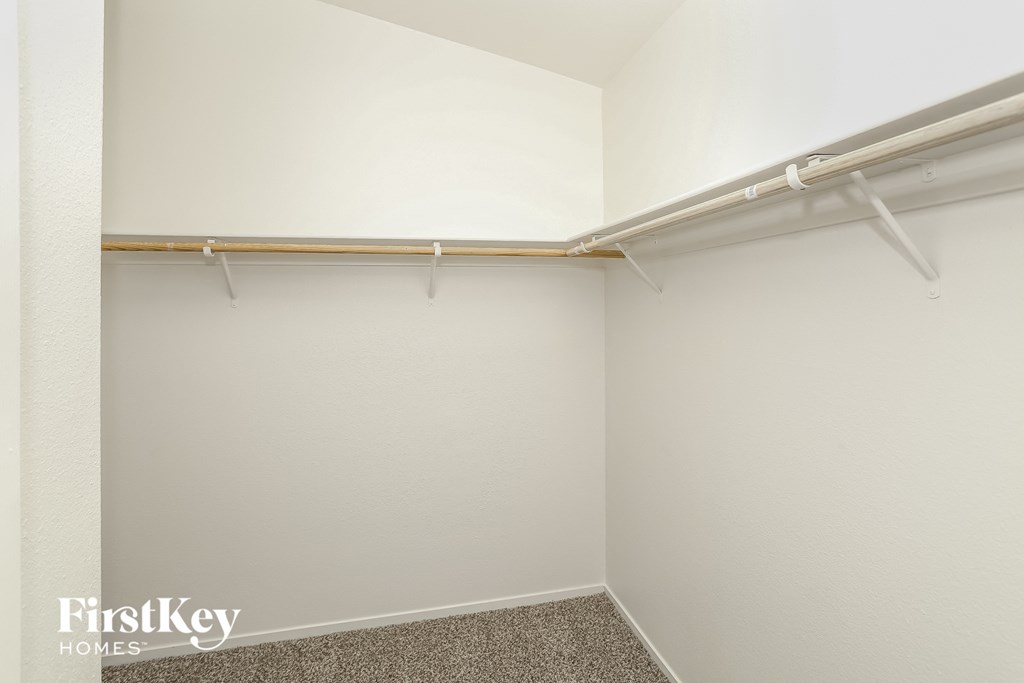 a walk in closet in a white room with a white wall and a metal pipe