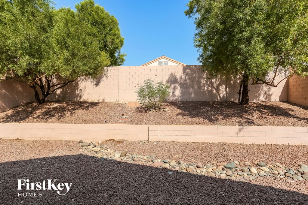 a backyard with gravel and trees and a retaining wall