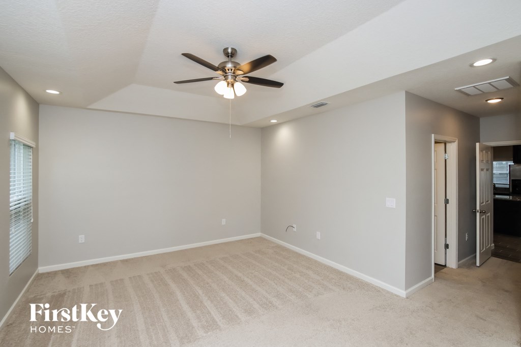 A spacious room with a ceiling fan and beige carpeting.