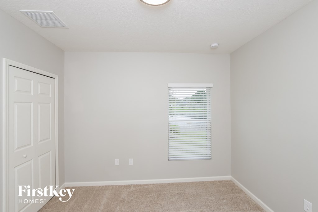 A room with a carpeted floor, a window with blinds, and a door.