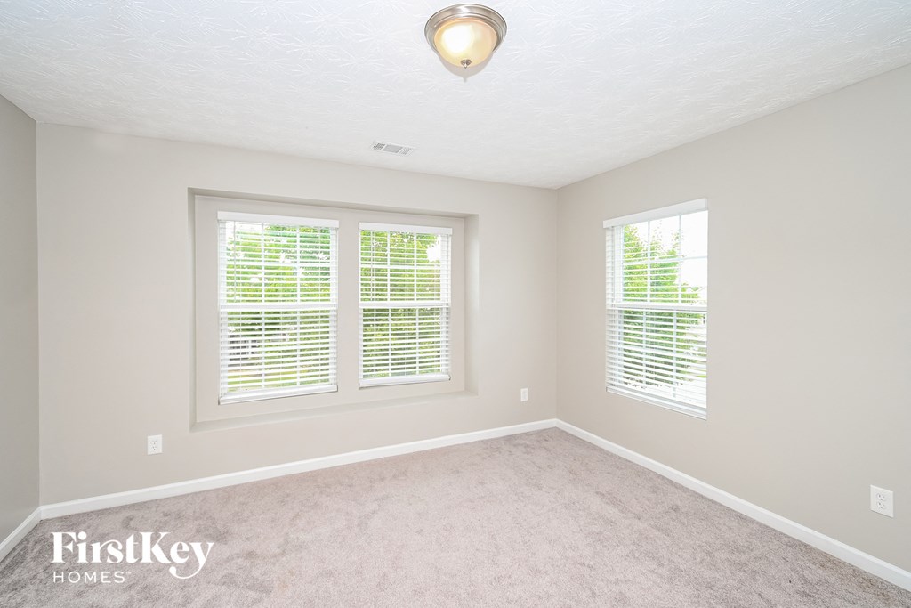 a bedroom with three windows and a carpeted floor