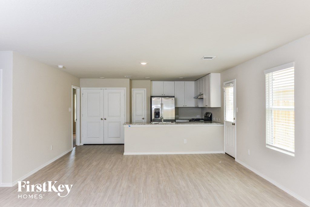an empty living room and kitchen with white cabinets and wood flooring