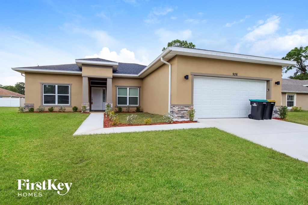 A beige house with a black trash bin and a white garage door.