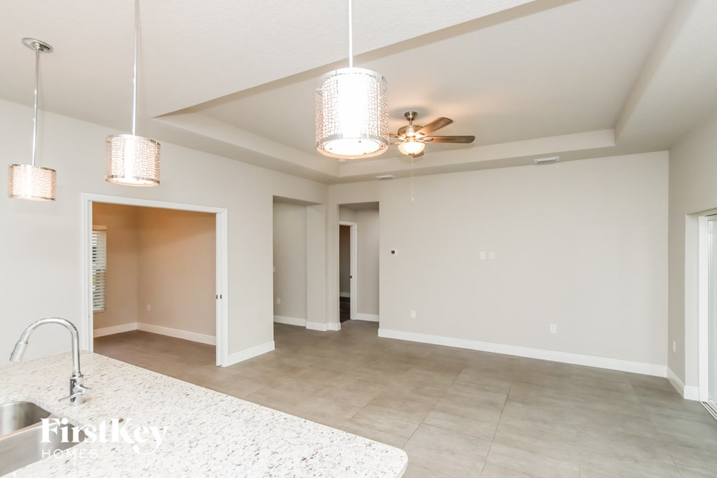 A spacious, empty room with a kitchen area and a ceiling fan.