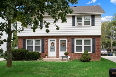 a white house with black shutters and a white door with a tree in front of it