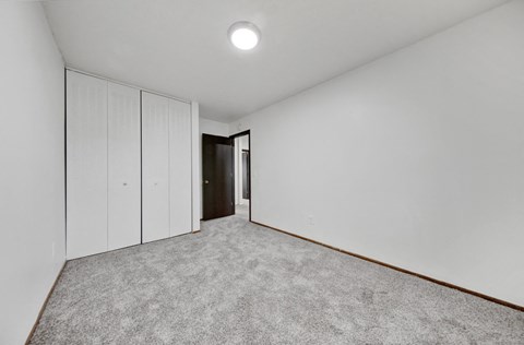 a bedroom with white walls and carpet and a door to a closet