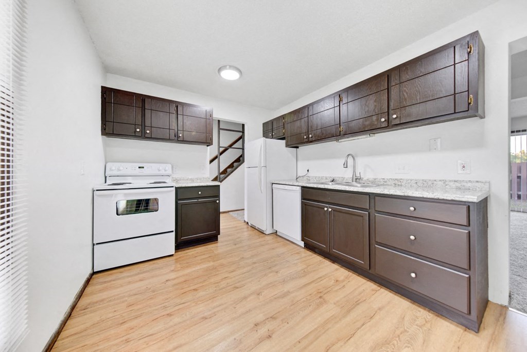 an empty kitchen with white appliances and wooden floors
