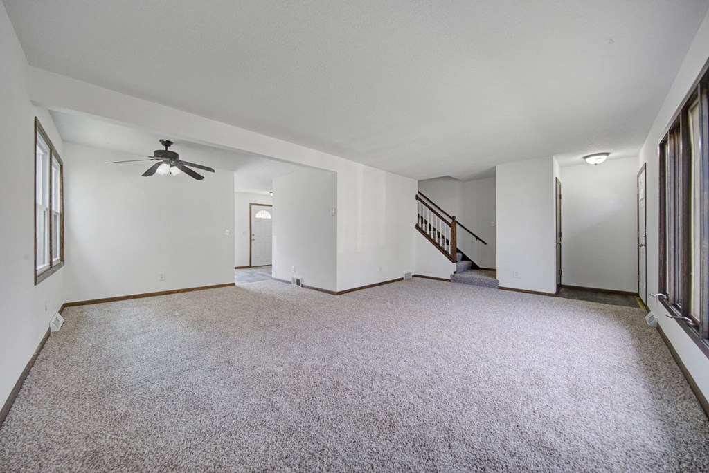 the living room is empty of furniture and has a ceiling fan