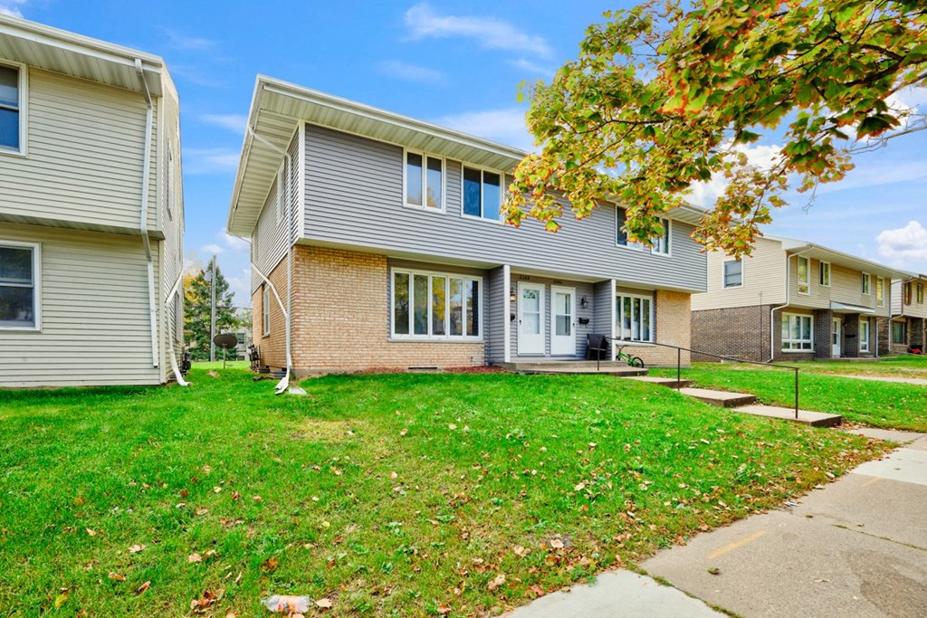 a white and brick house with a yard and sidewalk