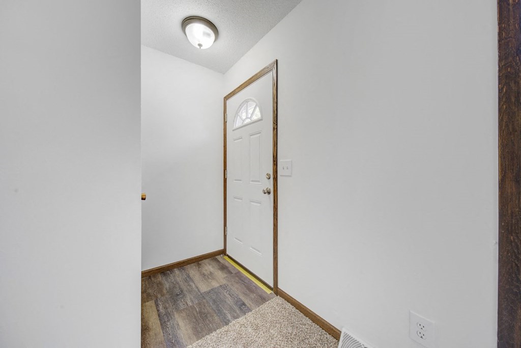 the entrance to a room with a white door and a hallway with wood flooring