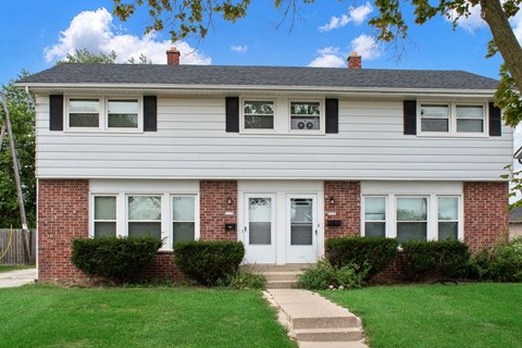A white house with a brick foundation and a white door.